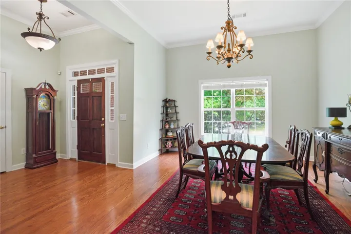 Hardwood floors flow through the inviting entry and formal dining area, illuminated by natural light and a classic chandelier.