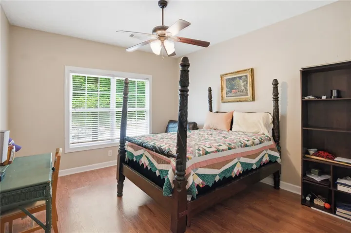 Hardwood flooring extends throughout this well-lit bedroom featuring a functional ceiling fan.