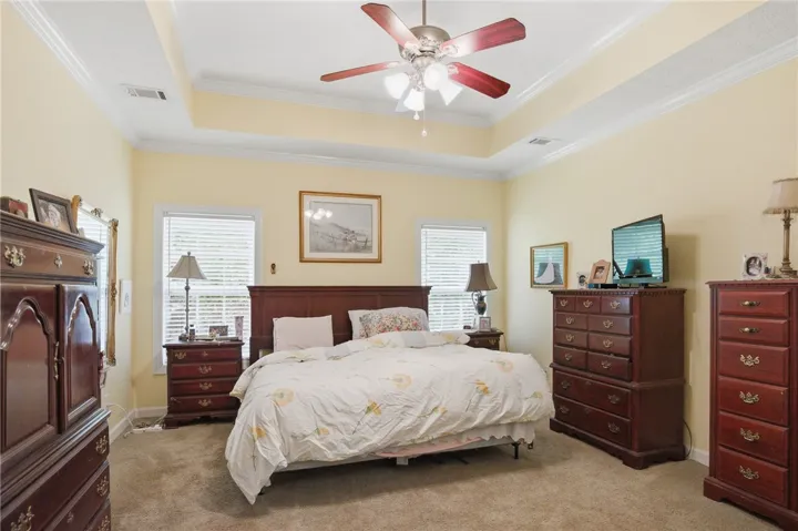 Relax in this tranquil bedroom, featuring a tray ceiling and soft, neutral carpeting.