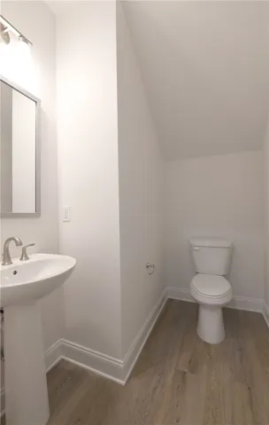 A minimalist powder room incorporates a pedestal sink and clean, modern flooring under a sloped ceiling.