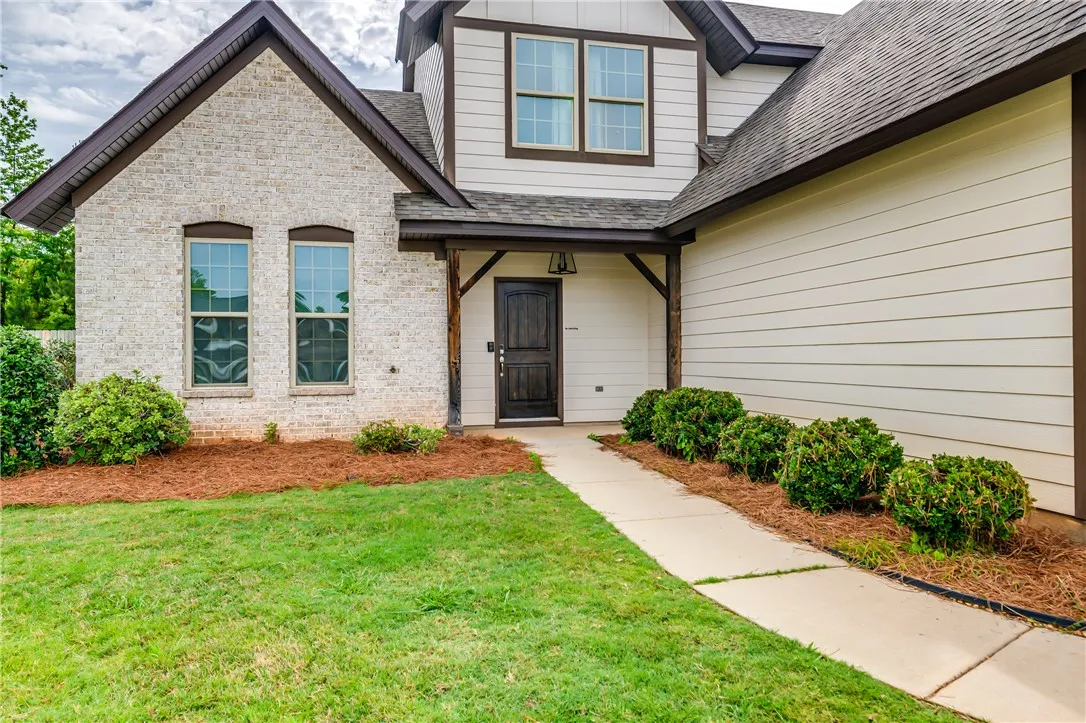 A welcoming entry features a dark wood door, contrasting with the light brick and siding facade.