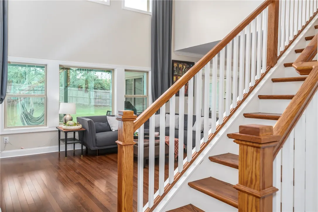 Rich hardwood flooring leads to a grand staircase and sun-filled living space with outdoor views.