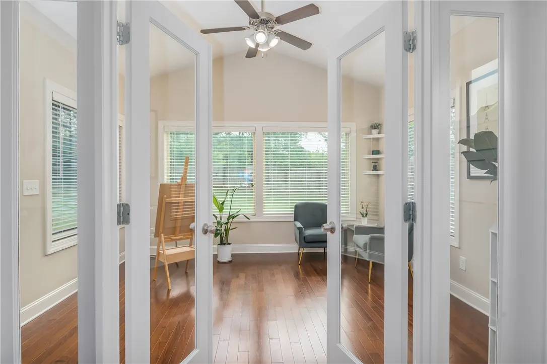 French doors open to a naturally illuminated sunroom, featuring a vaulted ceiling and rich hardwood flooring.