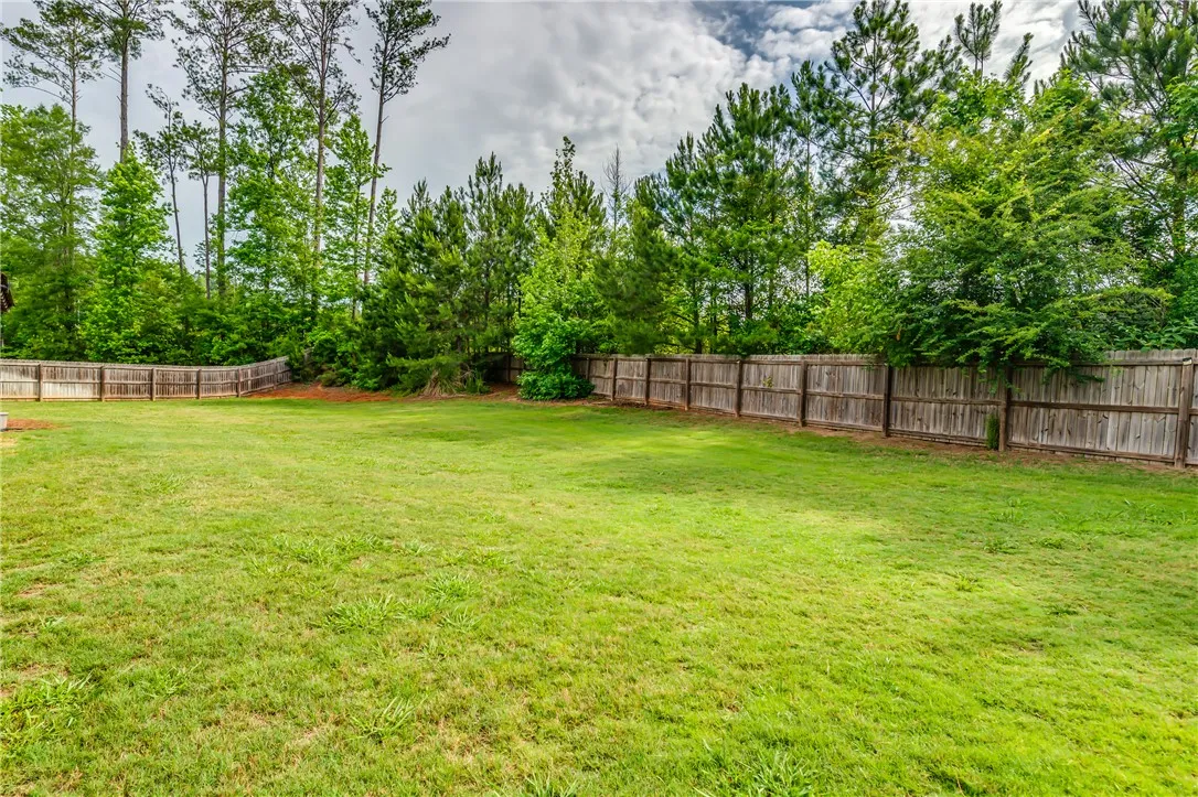 A spacious, verdant yard, fully fenced for privacy, bordered by mature trees under an open sky.