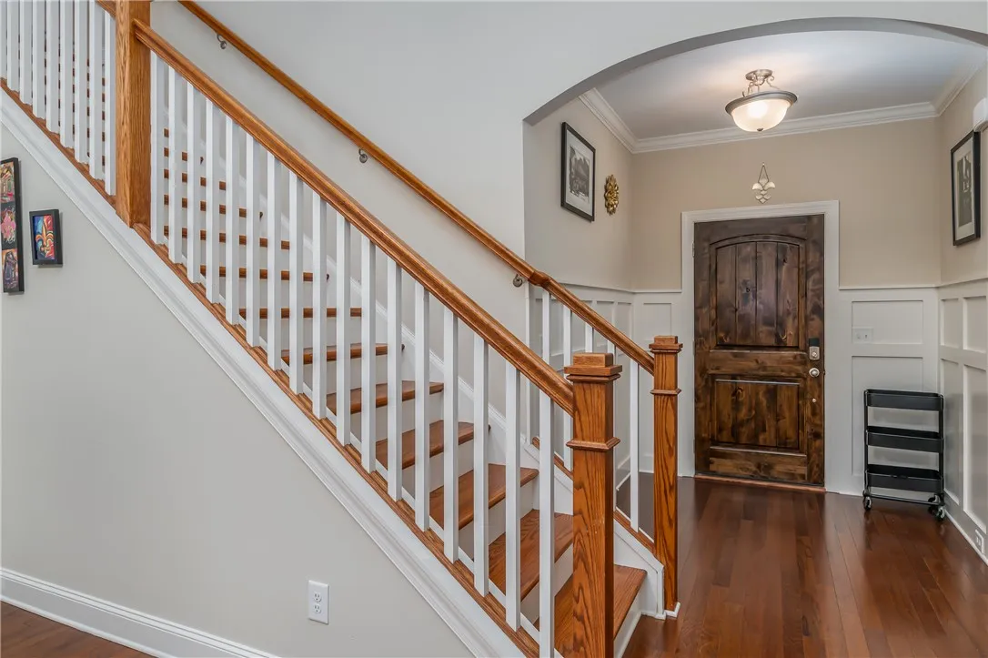 Rich hardwood floors welcome you into this elegant foyer, featuring a graceful staircase with traditional balusters and a dark wood entry door.
