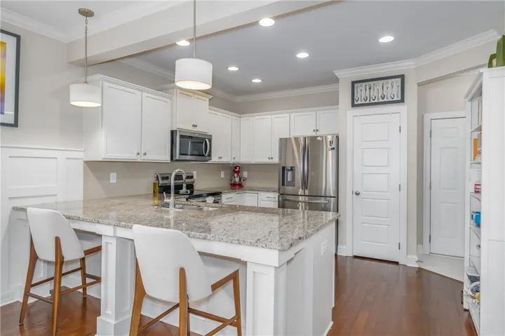 A sleek kitchen features an eat-in island with granite counters, stainless steel appliances, and rich hardwood flooring.