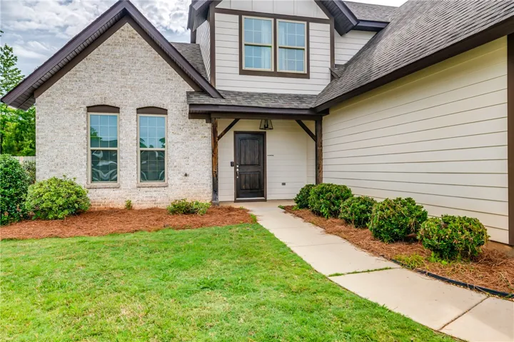 A welcoming entry features a dark wood door, contrasting with the light brick and siding facade.