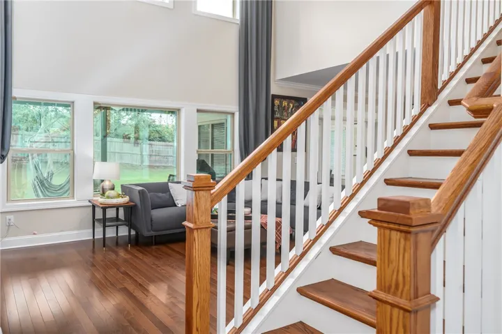 Rich hardwood flooring leads to a grand staircase and sun-filled living space with outdoor views.