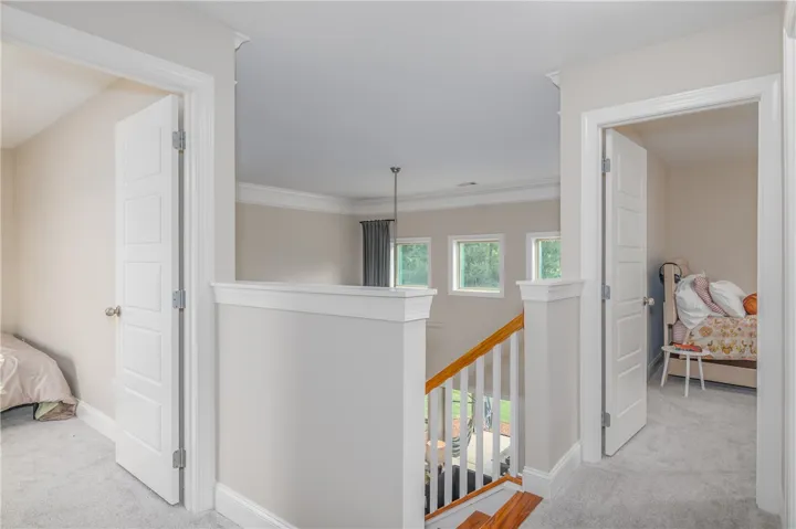 Upper-level landing offers carpeted floors and a view of the outside through well-placed windows.