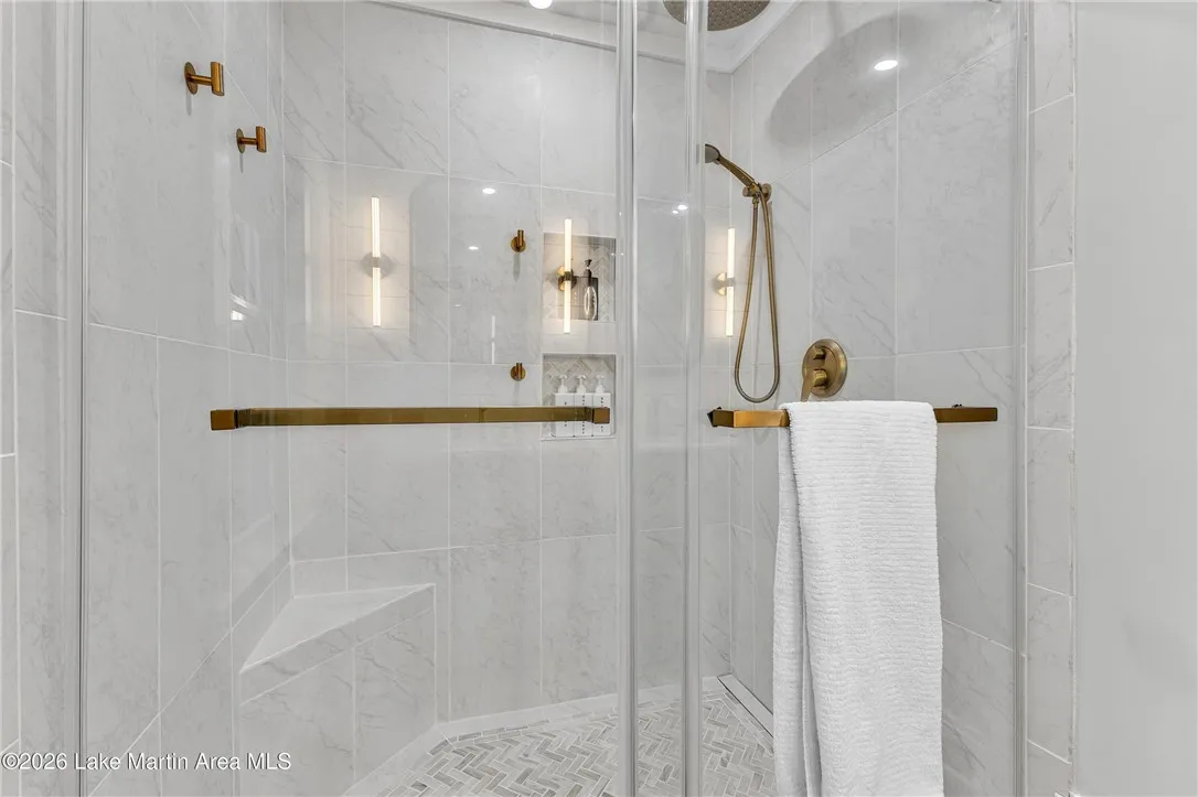 Luxurious walk-in shower with refined gold-toned fixtures and built-in shelving.