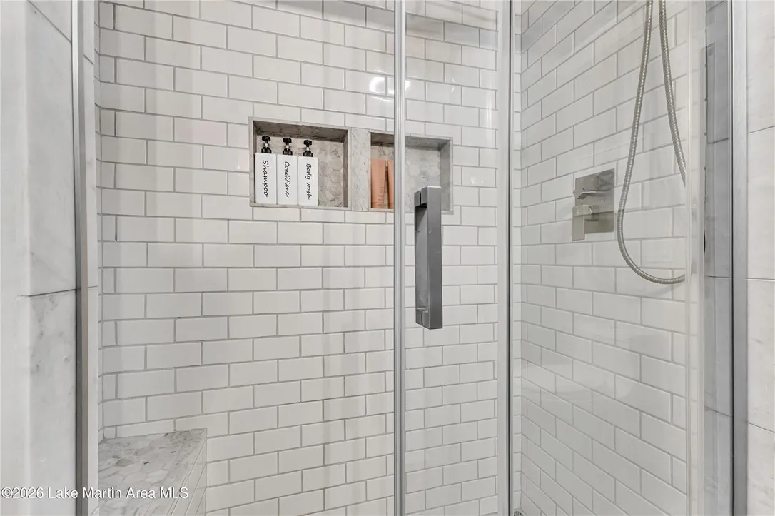 A pristine glass-enclosed shower showcases clean white subway tile and a built-in niche for toiletries.