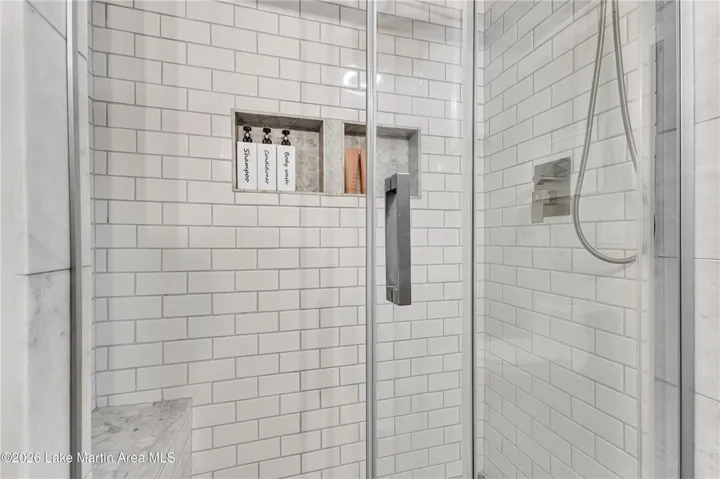 A pristine glass-enclosed shower showcases clean white subway tile and a built-in niche for toiletries.