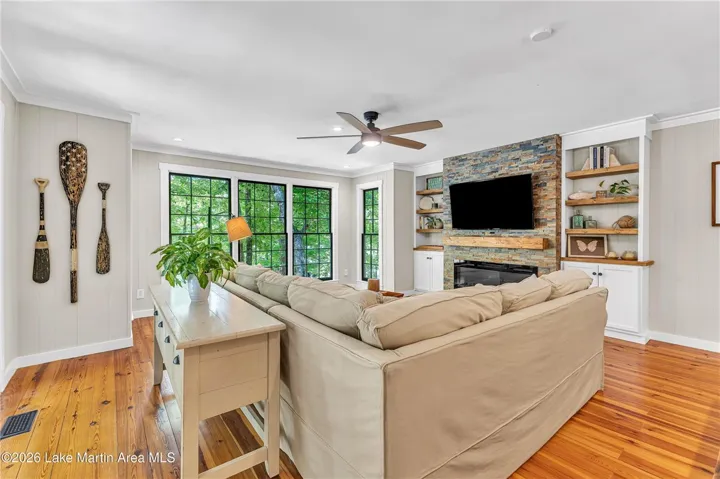 Luminous living area showcasing built-in shelving, a natural stone fireplace, and polished hardwood flooring.