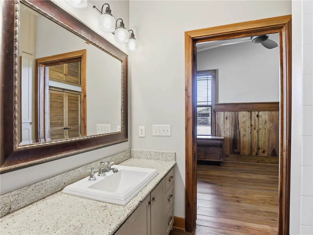 Granite counters and a framed mirror grace this functional bathroom, offering access to an adjacent room with wood flooring.