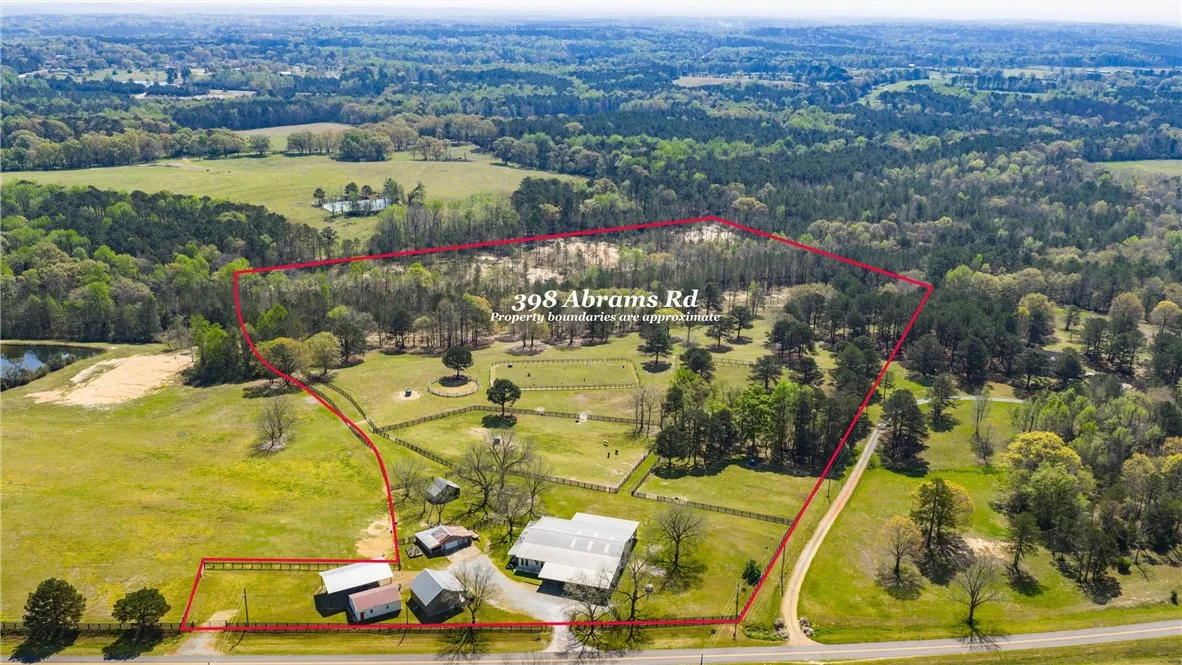 An expansive rural property, marked by a red boundary, encompasses a main residence, various outbuildings, and a serene pond.