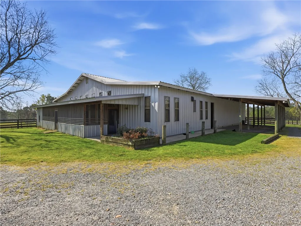 Metal-sided equestrian facility with an extended covered area and screened porch.