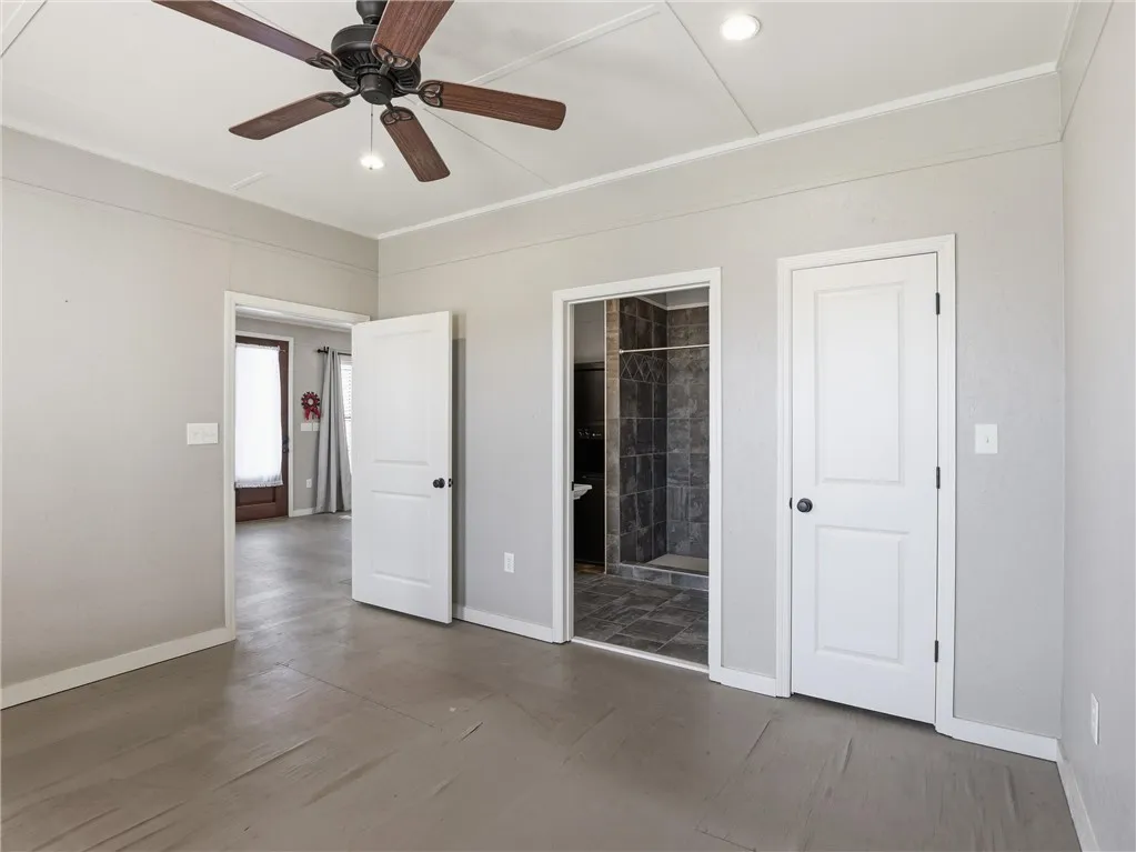 An airy bedroom with a ceiling fan offers direct access to an ensuite shower.