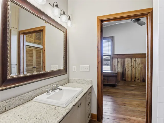Granite counters and a framed mirror grace this functional bathroom, offering access to an adjacent room with wood flooring.