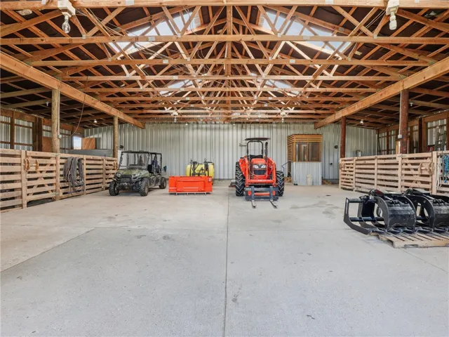 A spacious barn, ideal for equipment storage, features sturdy exposed wooden beams and a concrete floor.