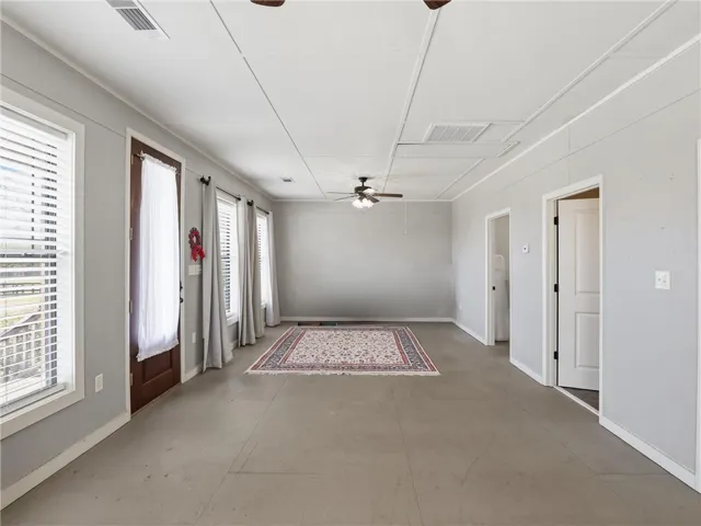 An inviting open-concept living space features a ceiling fan, numerous windows, and versatile flooring.
