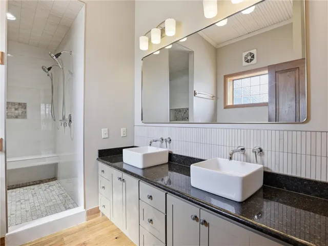 Dual vessel sinks adorn a spacious granite-topped vanity, complementing the modern walk-in shower with bench seating.