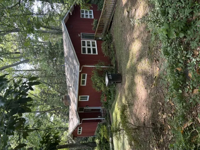 A private, verdant setting surrounds this charming red siding house with mature trees and a rustic deck.