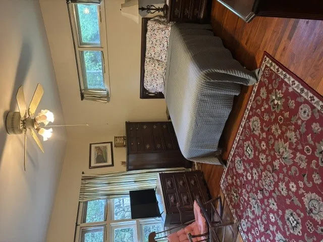 Hardwood flooring grounds this comfortable bedroom, featuring ample natural light and a practical ceiling fan with illumination.