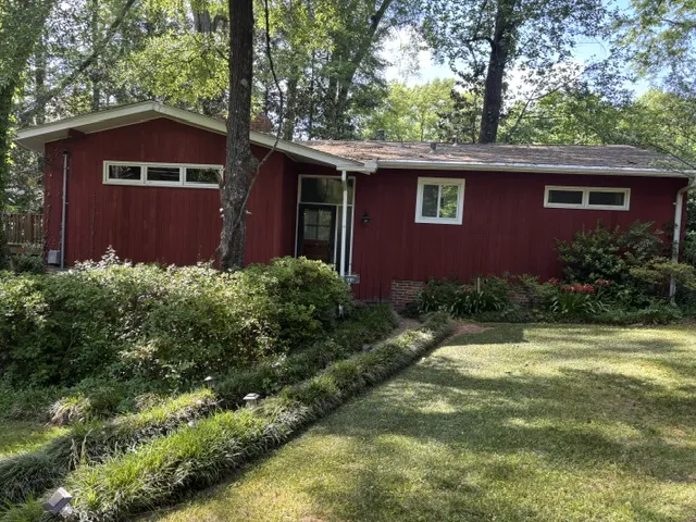 A well-maintained lawn and verdant landscaping complement this charming red exterior home.