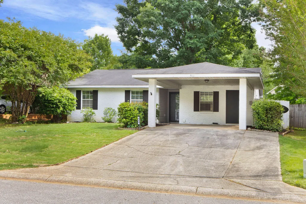 White brick home with black shutters, mature landscaping, and a convenient covered carport.