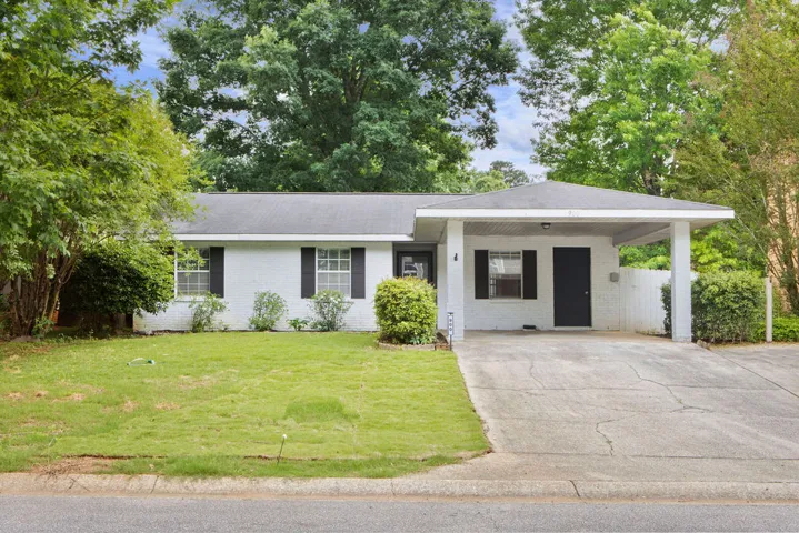 A classic ranch home features a covered carport and a spacious front lawn, framed by mature trees.