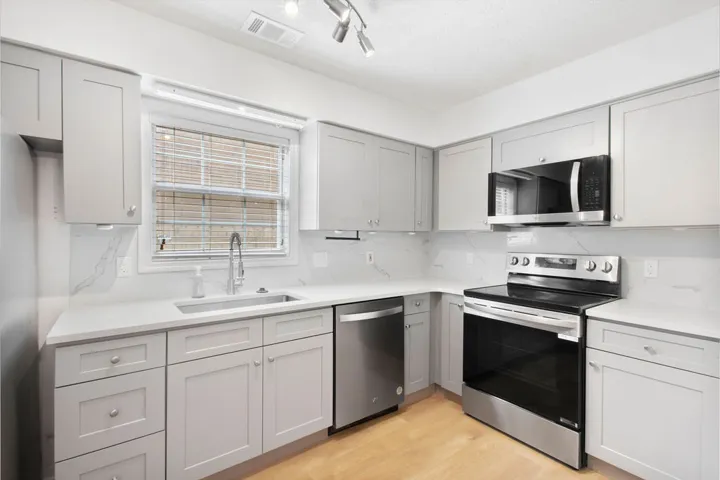 Brightly illuminated with recessed lighting, this kitchen features sleek gray cabinetry and stainless steel appliances.