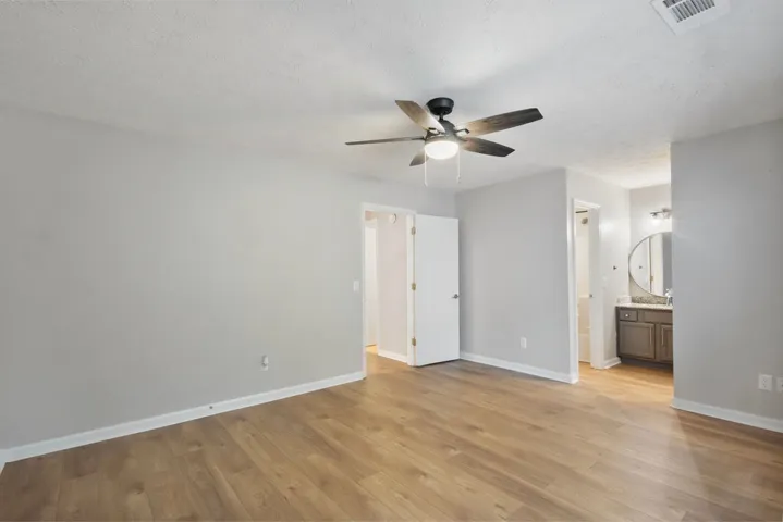 A tranquil primary suite with warm wood flooring and an attached private bath.