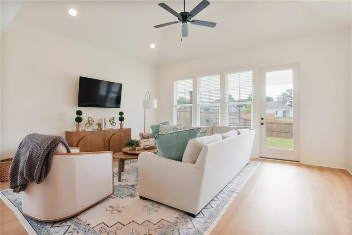 A well-lit living space features high ceilings and wood flooring, opening to an outdoor area through a glass door.