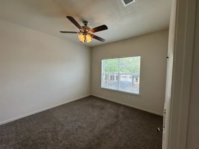 A well-lit primary bedroom featuring a ceiling fan, plush carpeting, and a window for natural light.