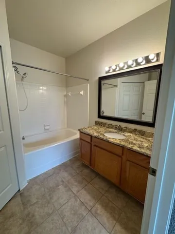 A well-lit primary bathroom features a functional vanity with ample storage and a classic shower-tub combination.
