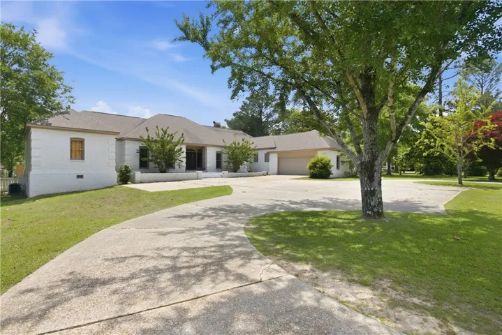A spacious driveway gracefully curves towards a charming white brick residence, framed by mature trees and verdant landscaping.
