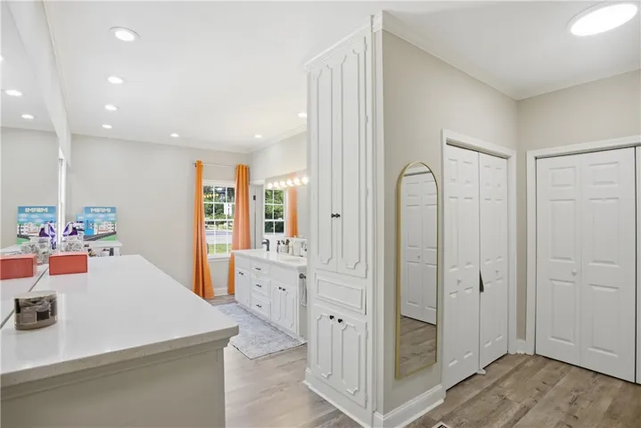 Recessed lighting illuminates this well-appointed bathroom featuring dual vanities, built-in storage, and durable wood flooring.