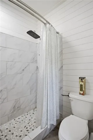 Marble-tiled shower with pebble flooring and a spacious overhead rain showerhead create a tranquil bathing experience.