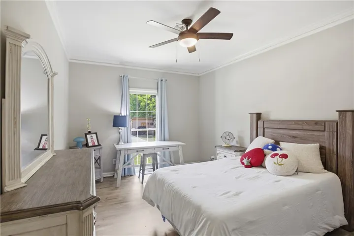 Relax in this well-lit bedroom featuring a ceiling fan and elegant crown molding.