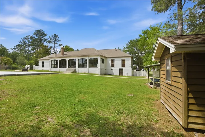 A spacious lawn unfolds before a captivating white brick home, complemented by a quaint wooden outbuilding.