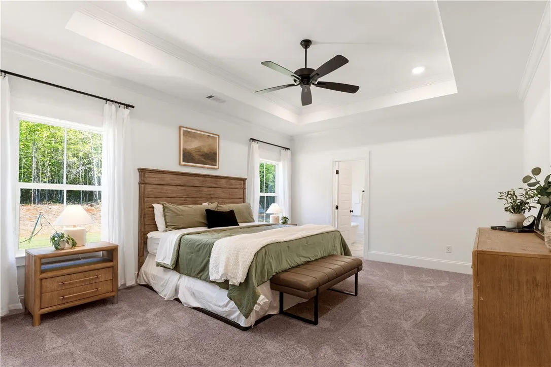 A tranquil primary bedroom with a spacious tray ceiling and verdant outdoor views.
