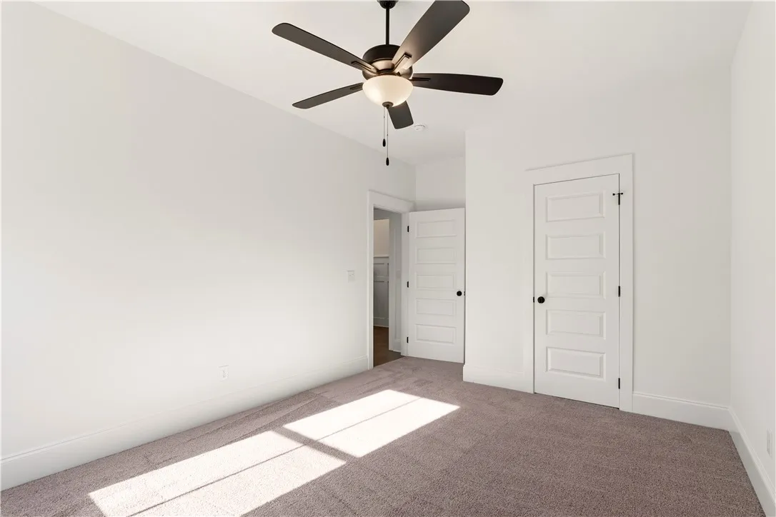 A spacious bedroom features plush carpet and an overhead ceiling fan.