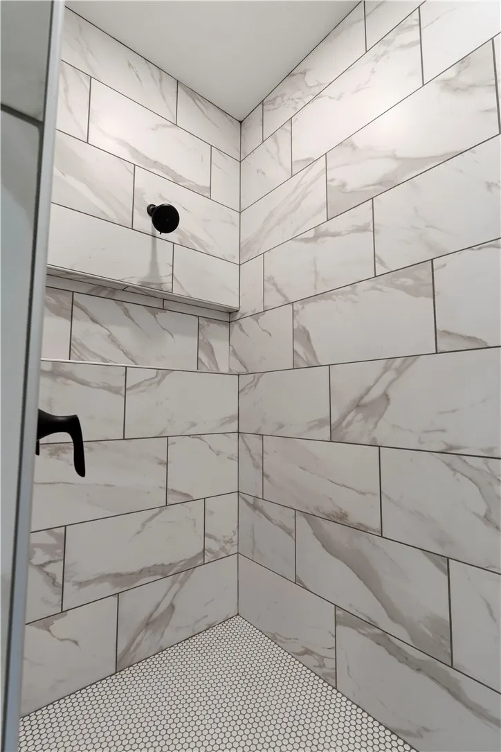 A pristine shower area featuring large format wall tiles and small hexagonal floor tiles.