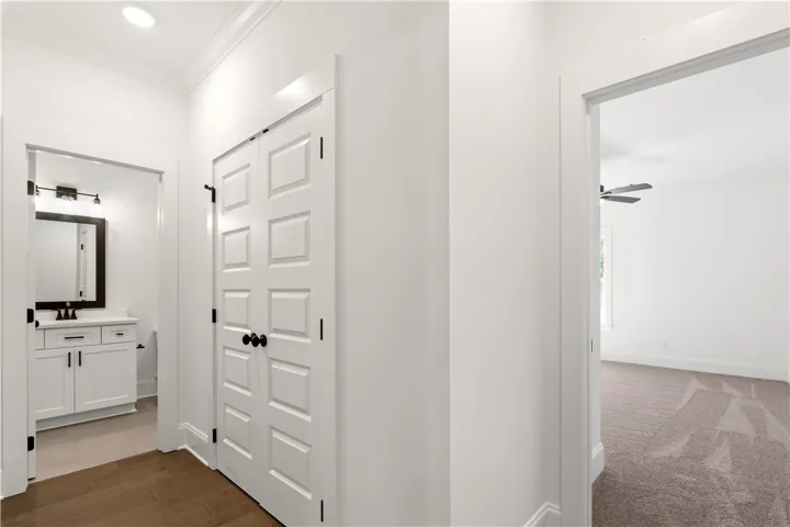 Hallway connecting to a naturally lit bedroom and a pristine bathroom vanity.