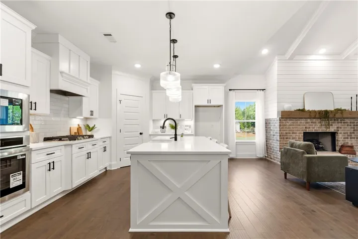 A well-lit kitchen with a spacious island flows into a cozy living area featuring a brick fireplace.
