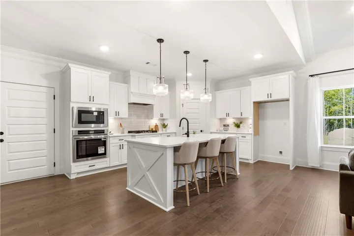 A pristine culinary space showcases a central island, rich hardwood flooring, and bright white cabinetry.