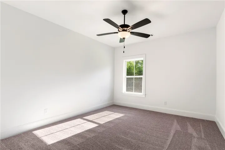 A well-lit bedroom with fresh carpeting and a window overlooking lush greenery.