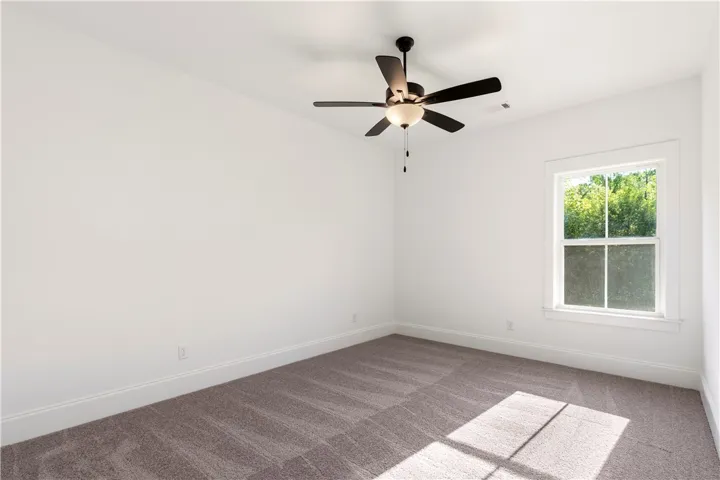 A well-lit bedroom features plush carpeting and a modern ceiling fan for ultimate comfort.