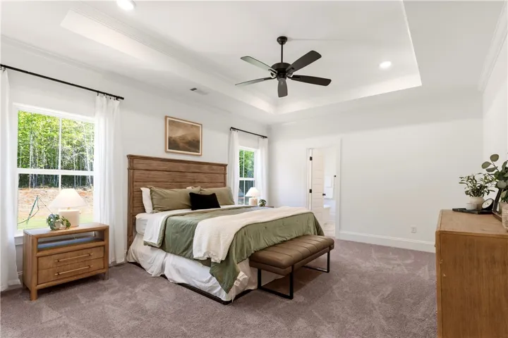 A tranquil primary bedroom with a spacious tray ceiling and verdant outdoor views.