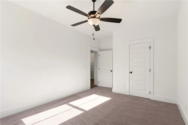 A spacious bedroom features plush carpet and an overhead ceiling fan.